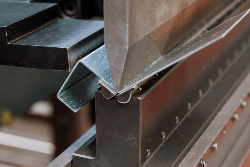 Détail d'une machine industrielle effectuant le pliage de tôle, montrant le métal en cours de formation à un angle précis.
