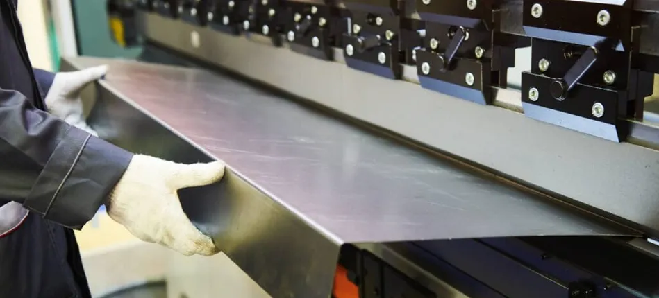 Opérateur industriel manipulant une grande feuille de métal dans une machine de pliage, illustrant les étapes précises du processus de pliage de tôle.